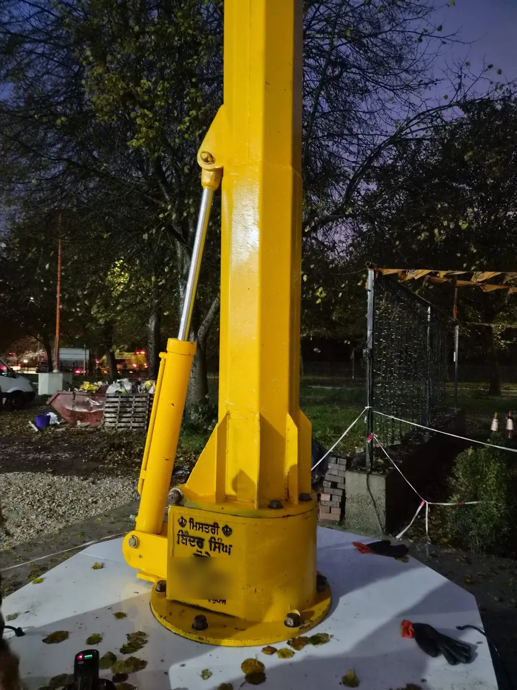 The yellow steel base of the Nishan Sahib with its hydraulic ram and the maker's inscription in Gurmukhi