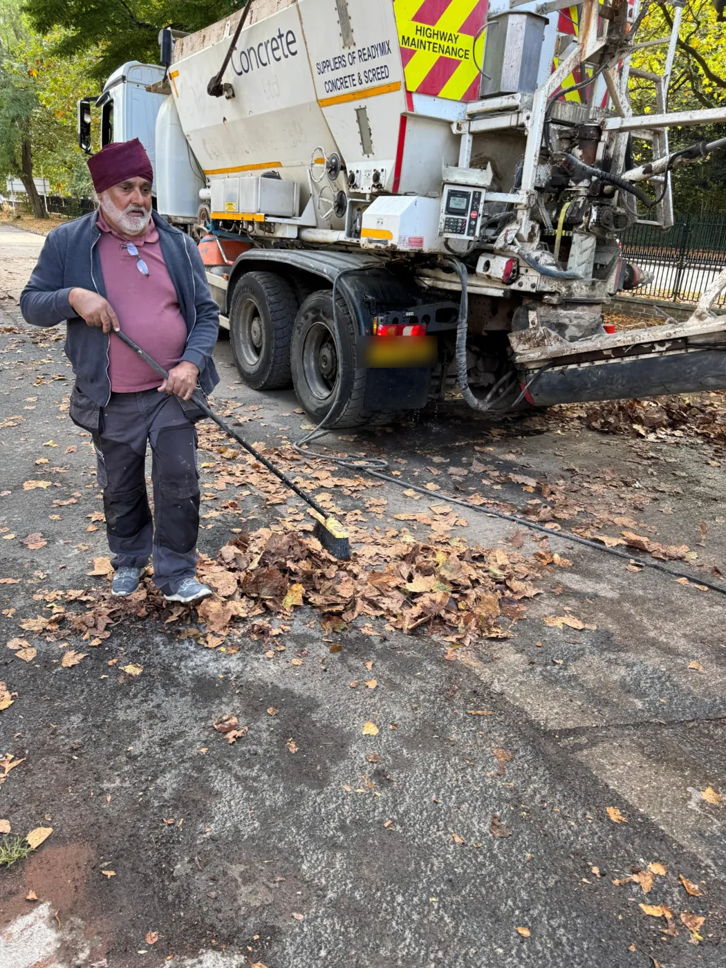 A sevadar sweeping leaves from the road beside a concrete lorry
