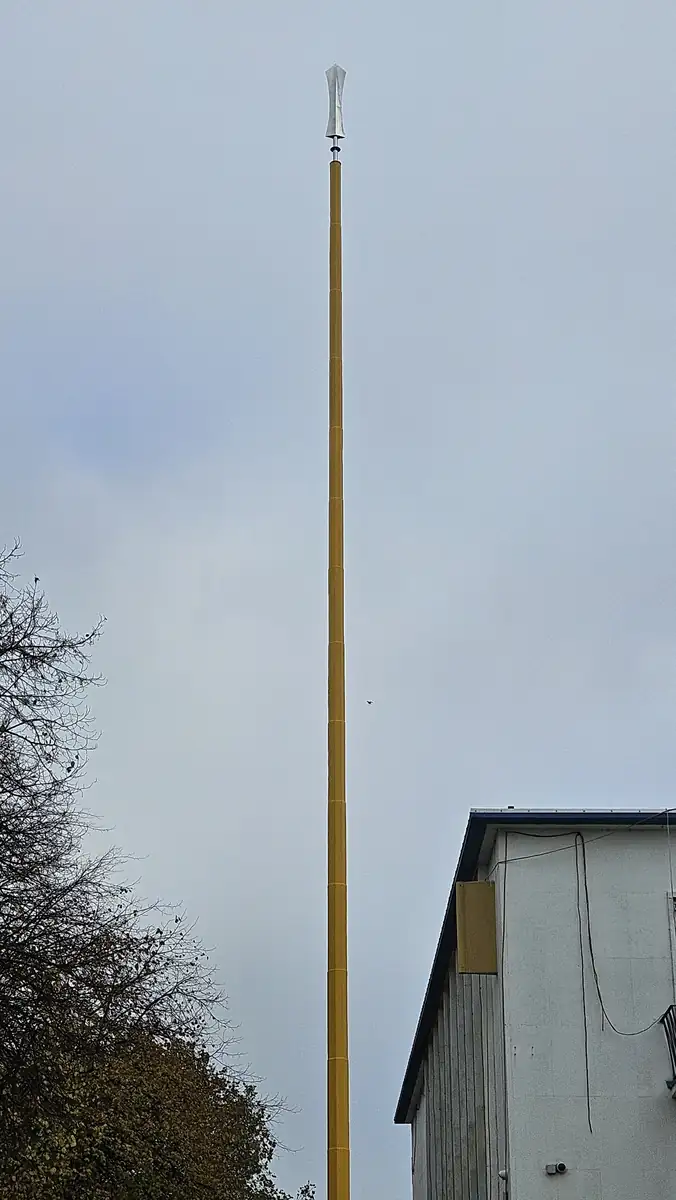 The bare yellow Nishan Sahib pole standing against a grey morning sky
