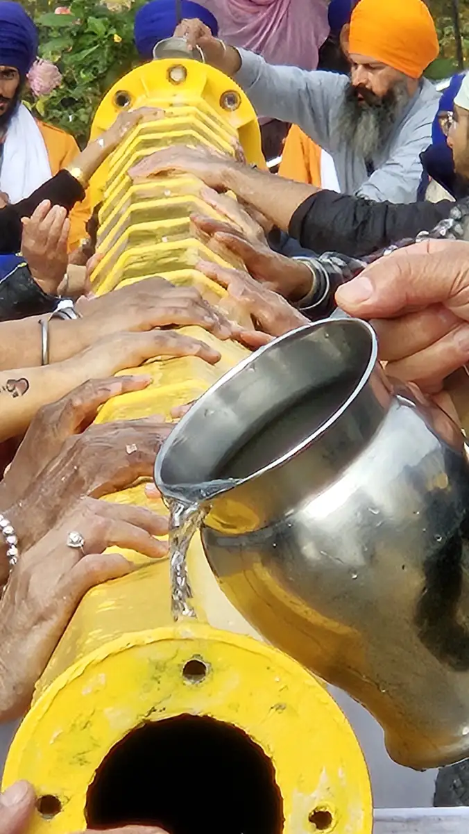 Many hands resting on the yellow pole as water is poured from a steel jug