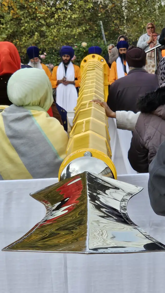 The polished steel Khanda on a white-covered table, with the sangat gathered behind