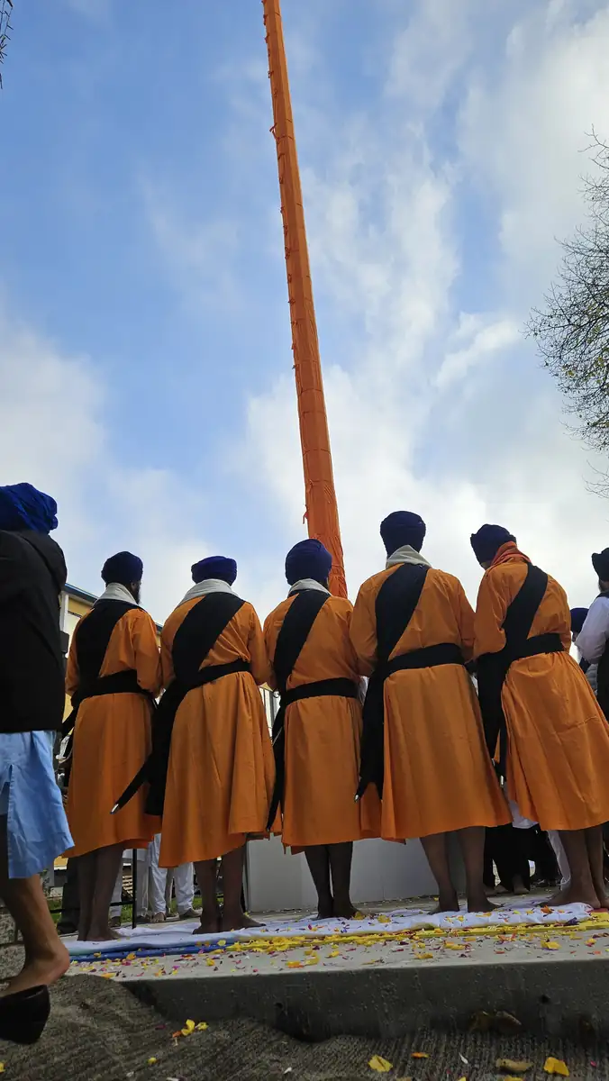 Looking up past the Panj Pyare in orange bana to the Nishan Sahib against a blue sky