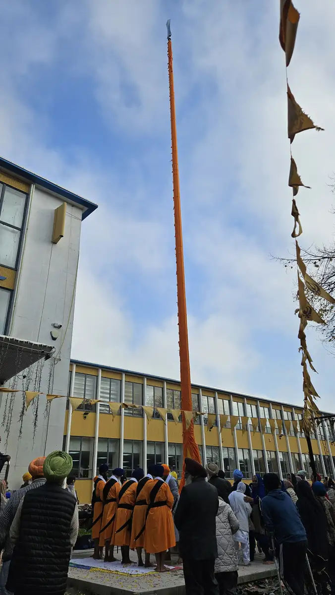The newly raised Nishan Sahib in its orange Chola Sahib, with the sangat and Panj Pyare at its base