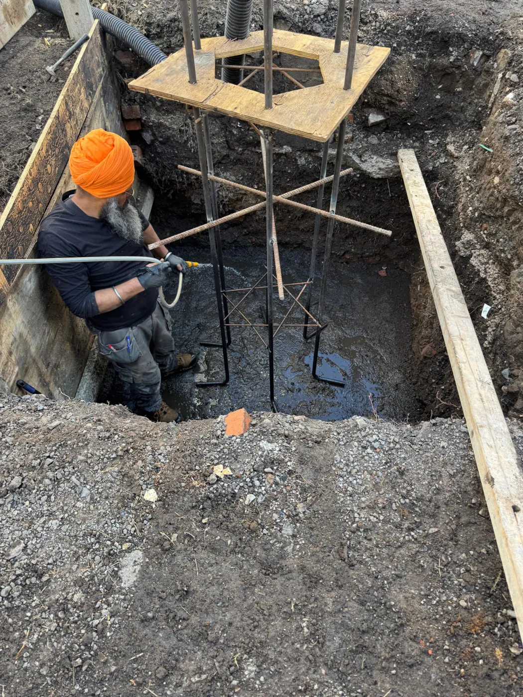 A sevadar in an orange dastaar preparing the reinforced foundation pit